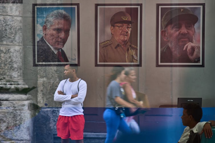 Three billboards of three men appear on a weathered wall outdoors.