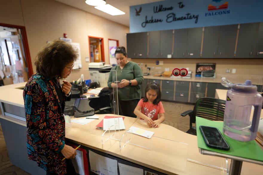 A Latino woman watches as another woman and a child work behind a reception desk.