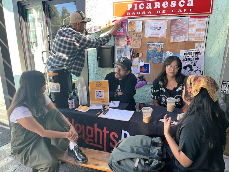 Photo of people sitting at a bench that has a Boyle Heights Beat tablecloth on it.