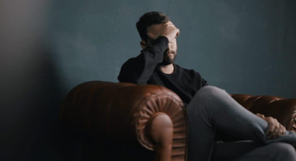 Struggling man with mental health issues sitting on a sofa in a dark room.