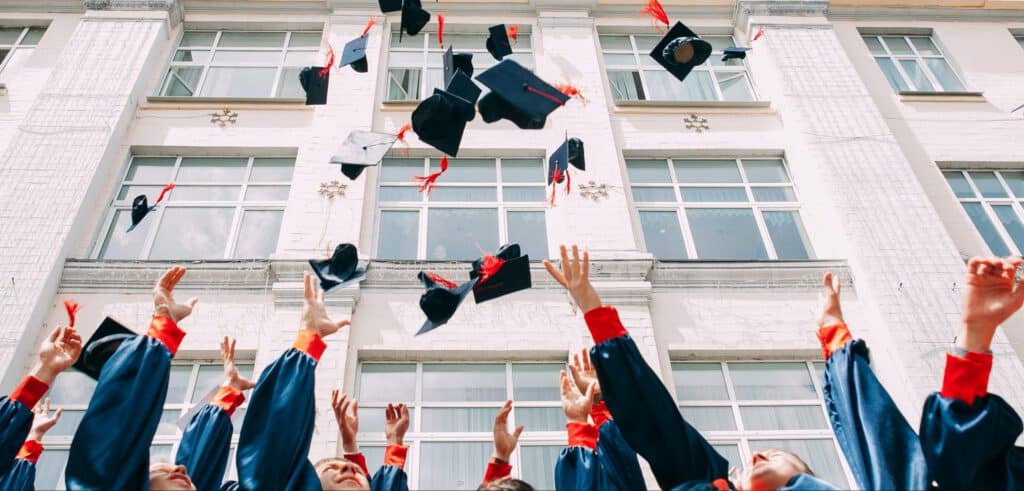 Graduates celebrating at Latino Summit 2022, throwing caps in the air outside a university building.