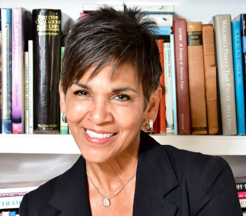 A woman smiling in front of a bookshelf filled with books, representing Marilyn Alverio.