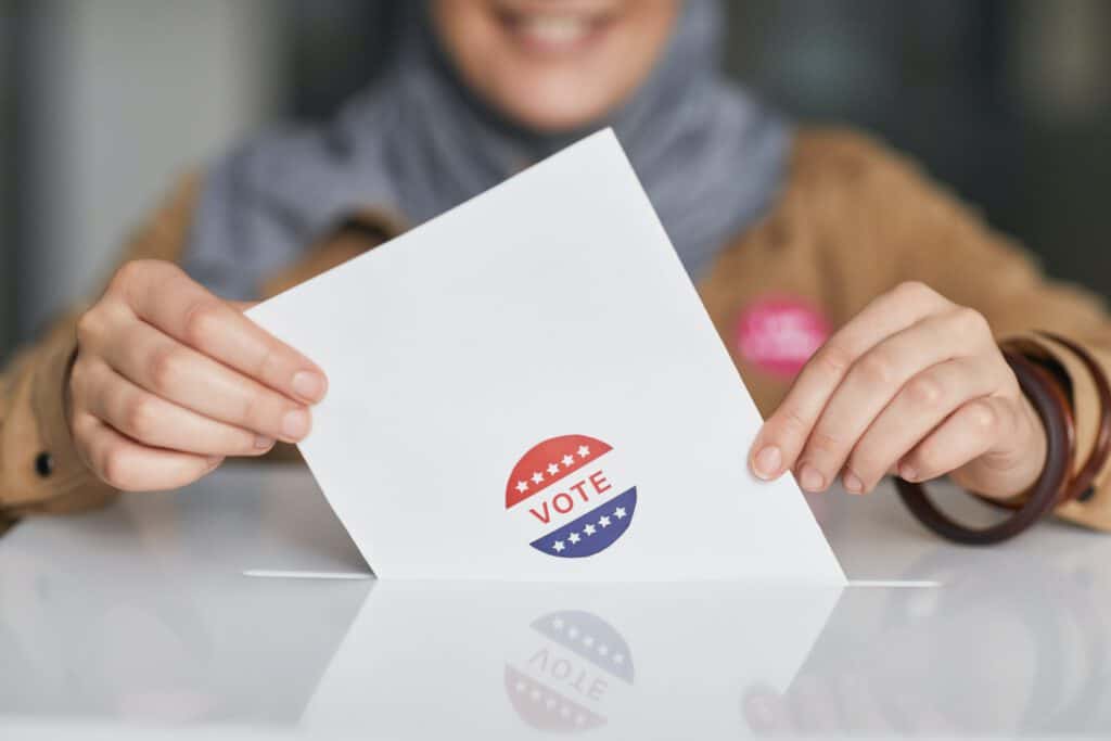 Voter casting ballot with "Vote" sticker, emphasizing Latino participation in elections.