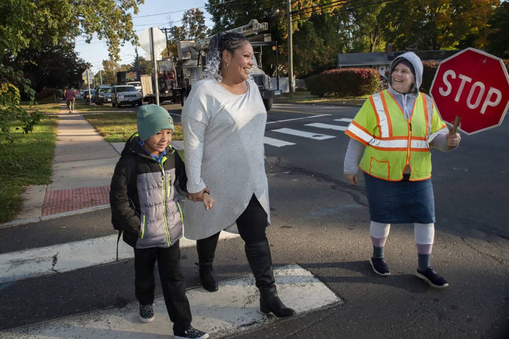 Child and adult crossing guard assisting children at a crosswalk.