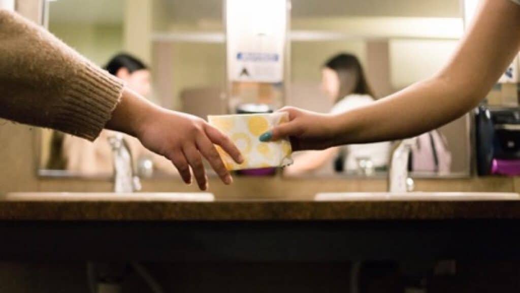 Two people exchanging a menstrual hygiene product during community discussion.