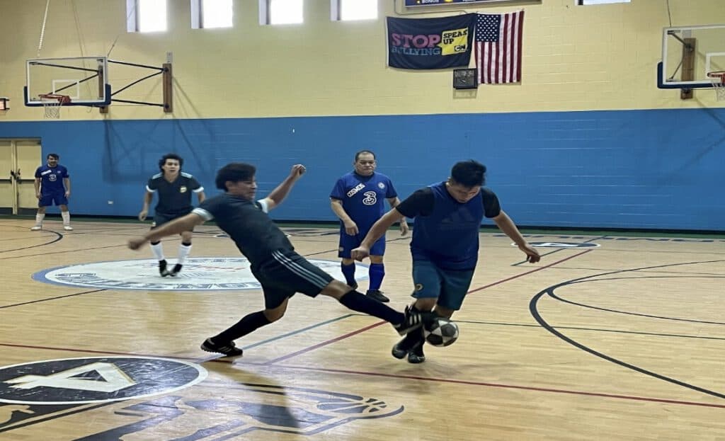Young Latino players competing in a youth soccer game in Chicago gymnasium.