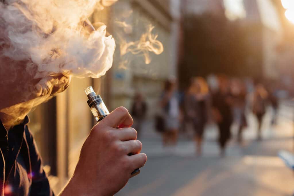 Vaping by a young person on a city street during sunset, highlighting youth nicotine exposure risks.