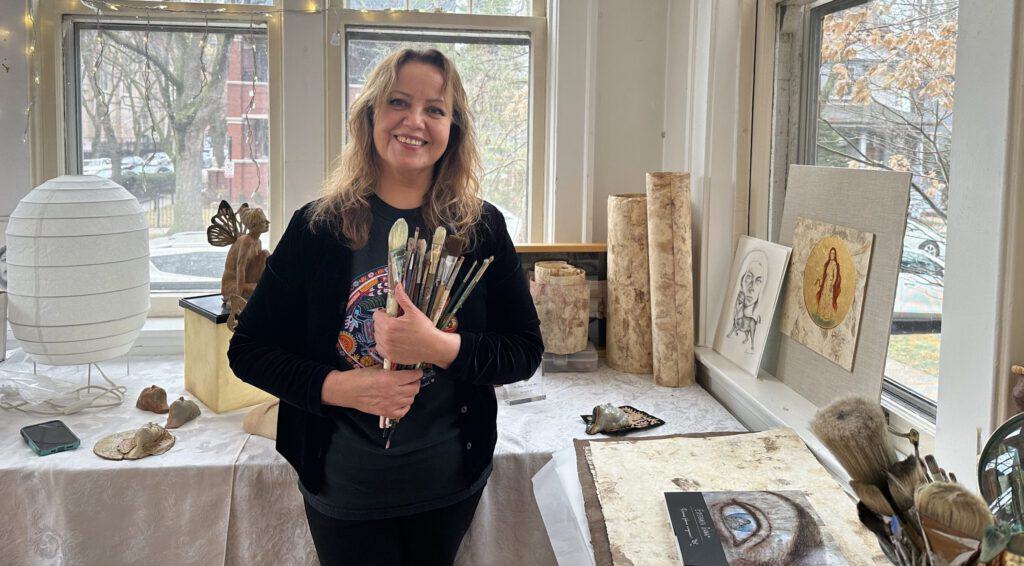 Esperanza Gama in her art studio surrounded by paintings and art supplies.