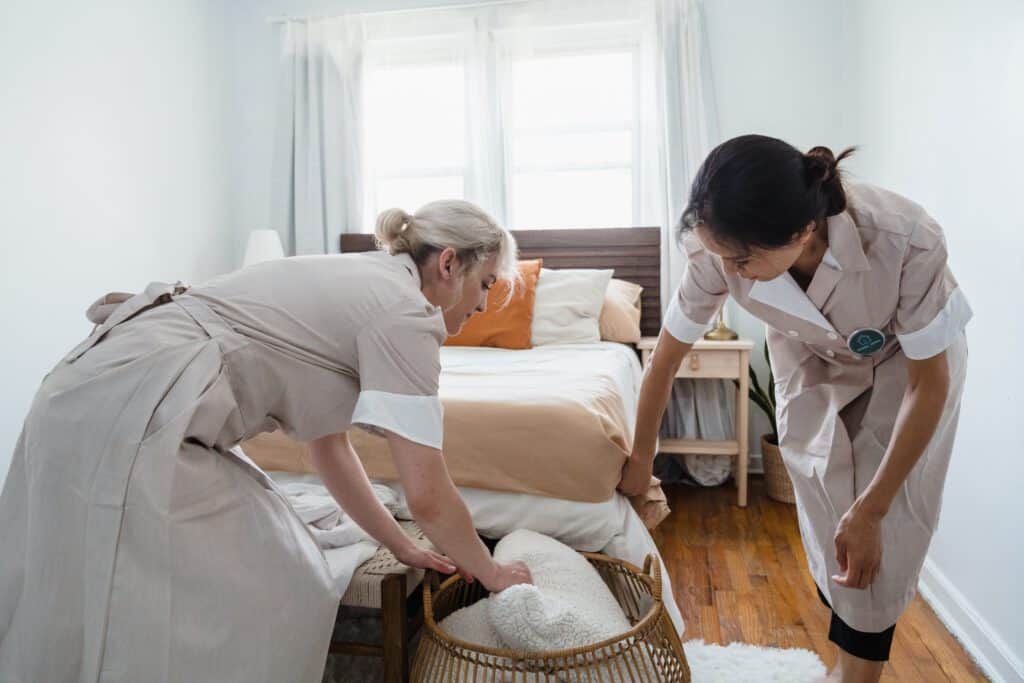 Cleaning staff disinfecting a bed in a hotel room, promoting hygiene and safety.