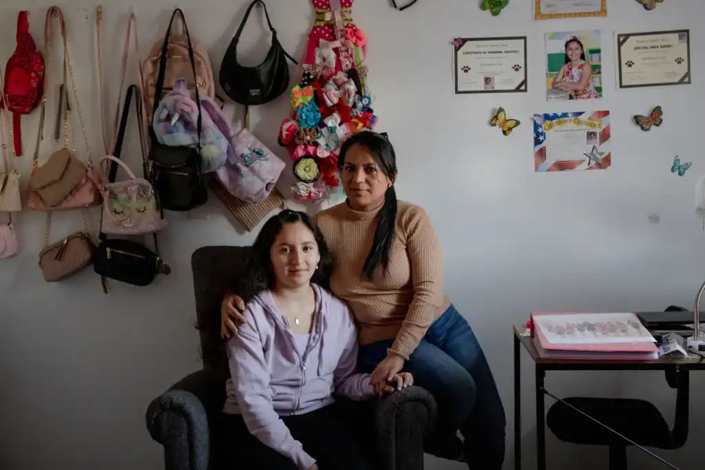 Woman and girl sitting in an office with bags and certificates on the wall.