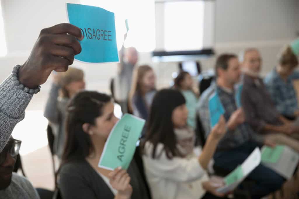 Disagree and agree signs held by diverse people at a community meeting on democracy.