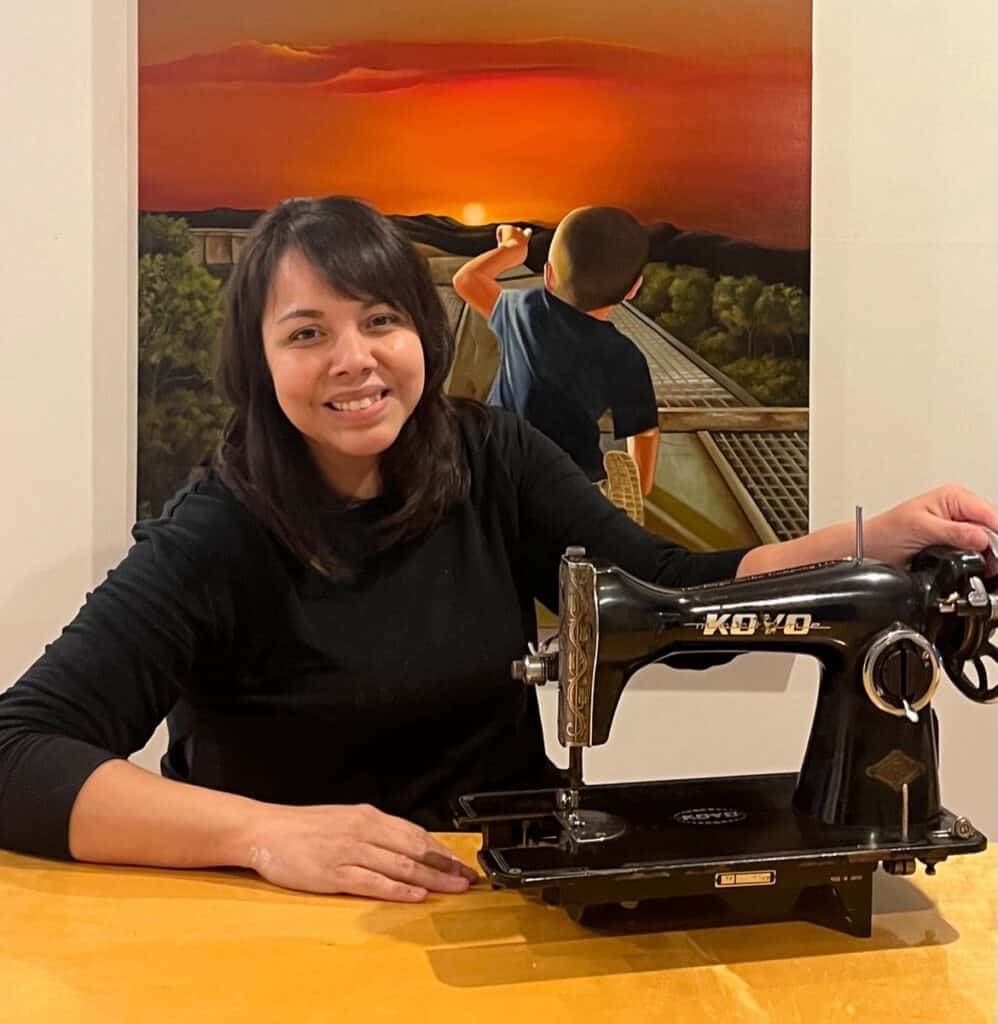 Sewing machine with woman and sunset mural in background, vibrant colors.