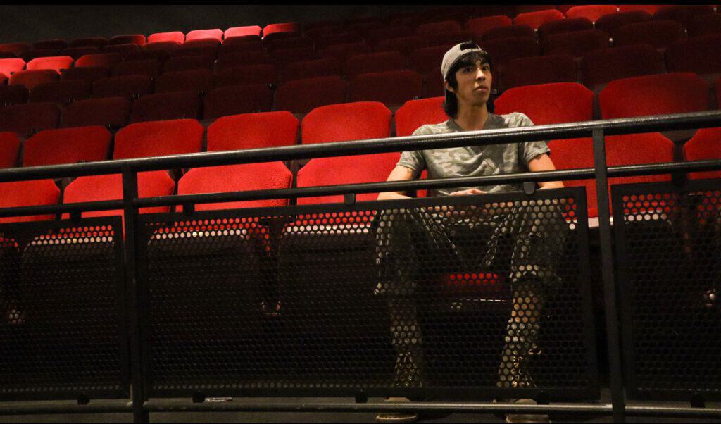 A woman sitting alone in an empty theater with red seats.