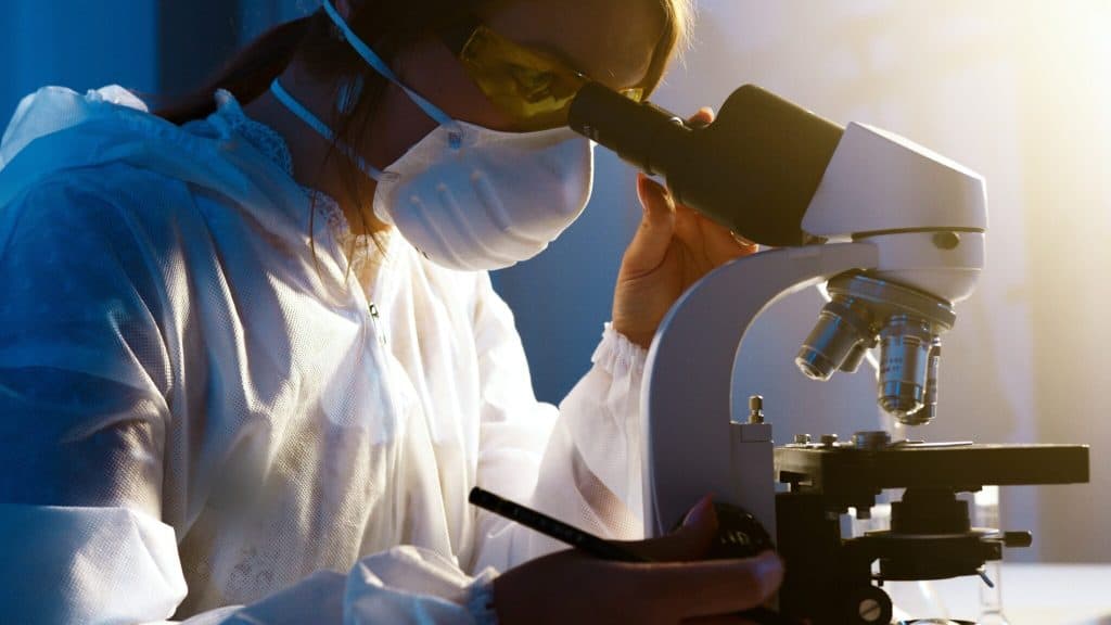 COVID-19 researcher examining samples with a microscope, focusing on long-COVID care for Latinos.