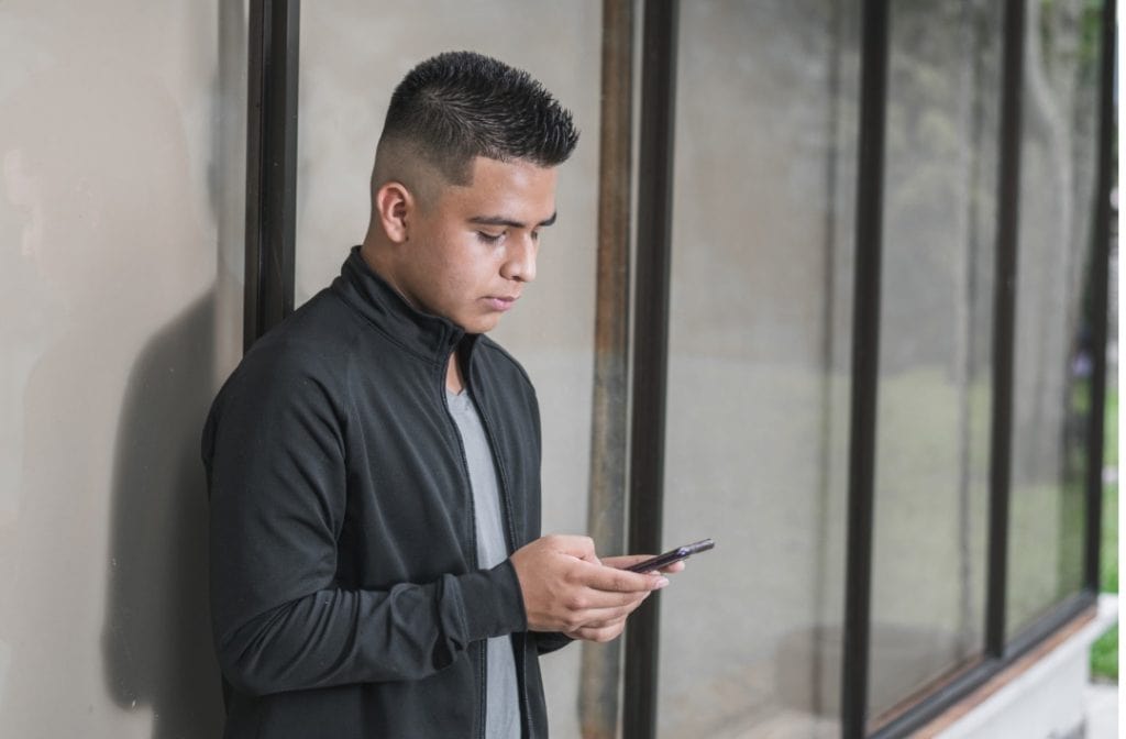 A young Hispanic man using a smartphone outdoors, reflecting news consumption habits among Latinos.