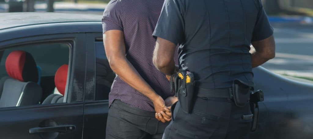Police officer detains a man near a car, highlighting immigration and racial profiling issues.