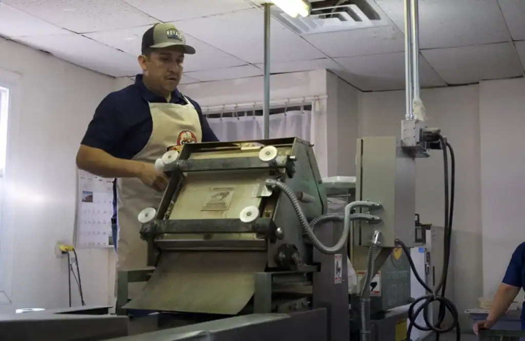 Immigrant worker operating industrial dough sheeter in a bakery in Kansas.