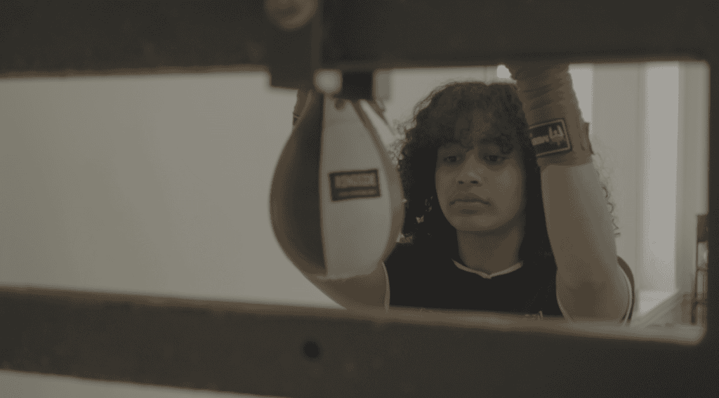 Afro-Latina female boxer training with gloves, focused on her upcoming fight in Washington Park.