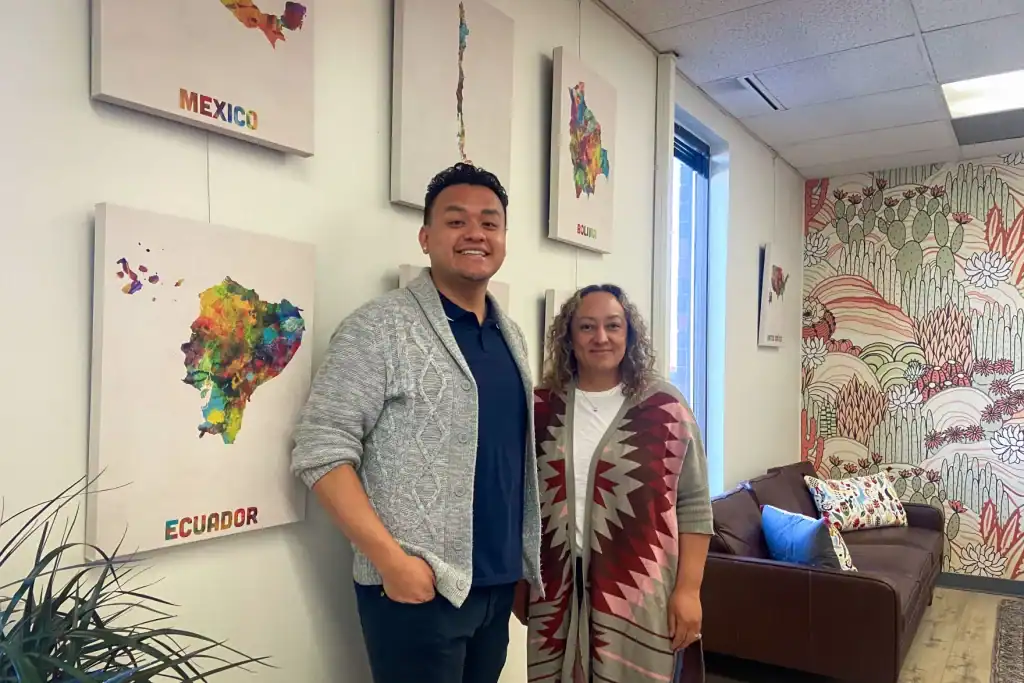 Latino man and woman in a community health center with colorful Latin American map art.