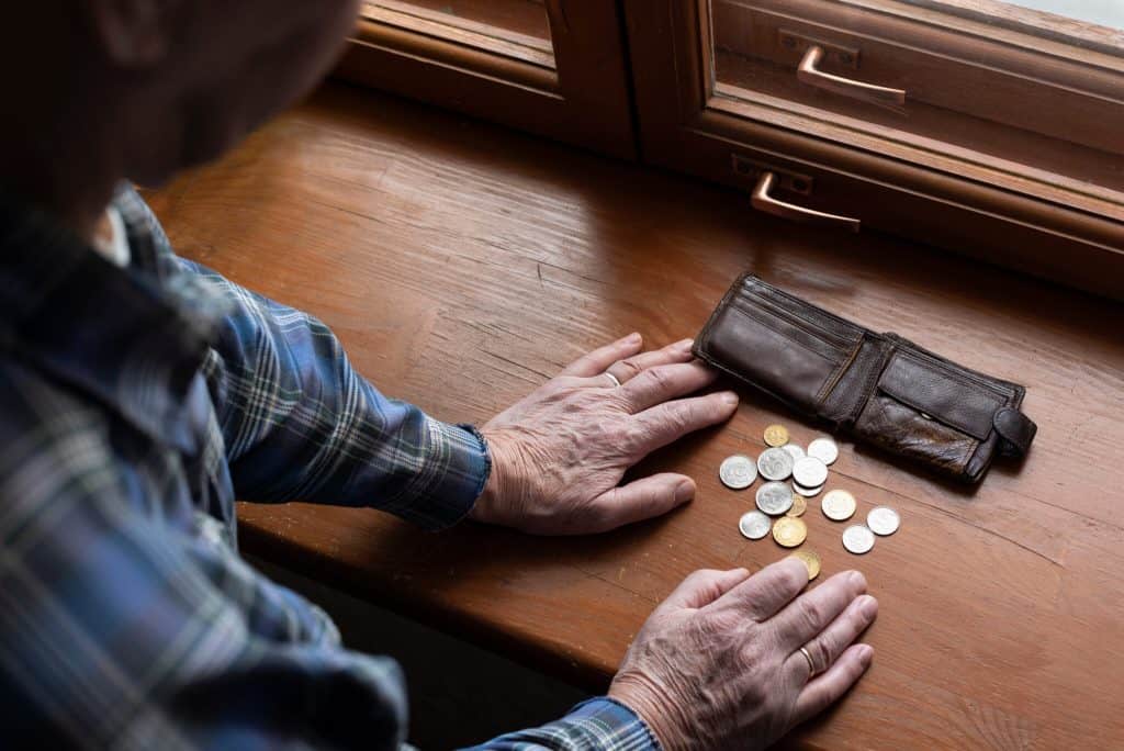 A person counting coins on a wooden surface near a window, highlighting financial struggles and econ.