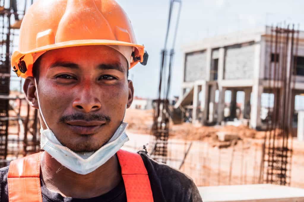 Construction worker wearing a safety helmet and mask at a building site.
