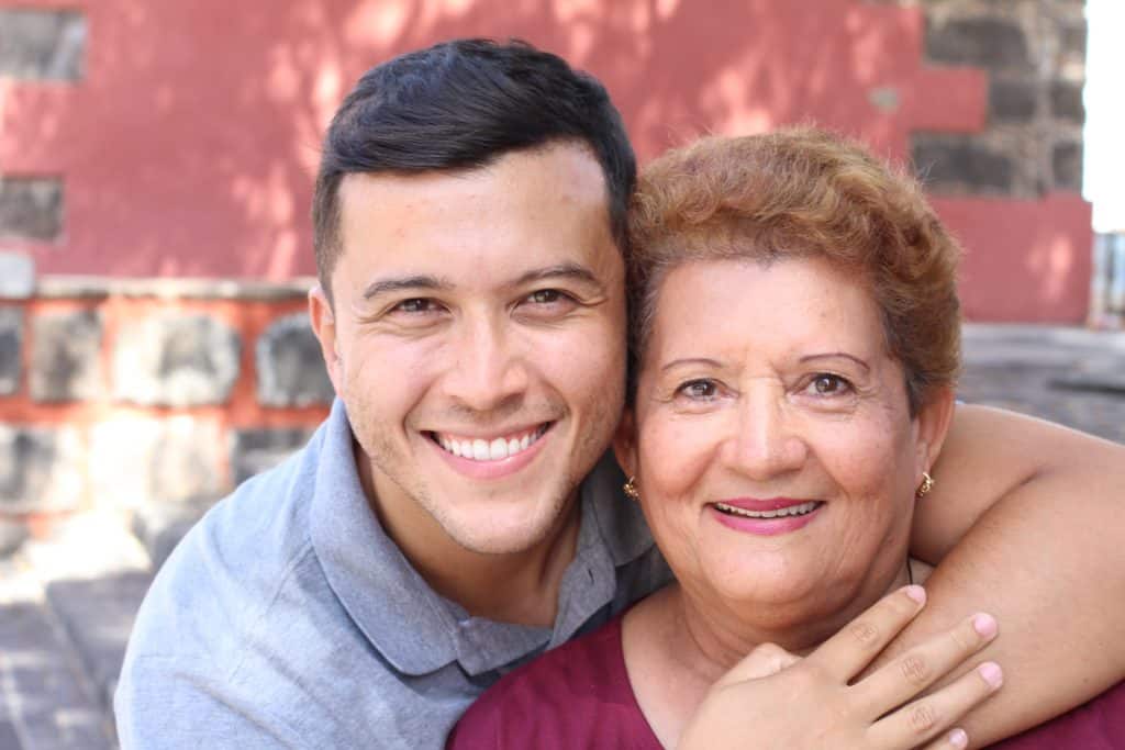 A woman and a young man smiling, embracing outdoors during Hispanic Heritage Month.