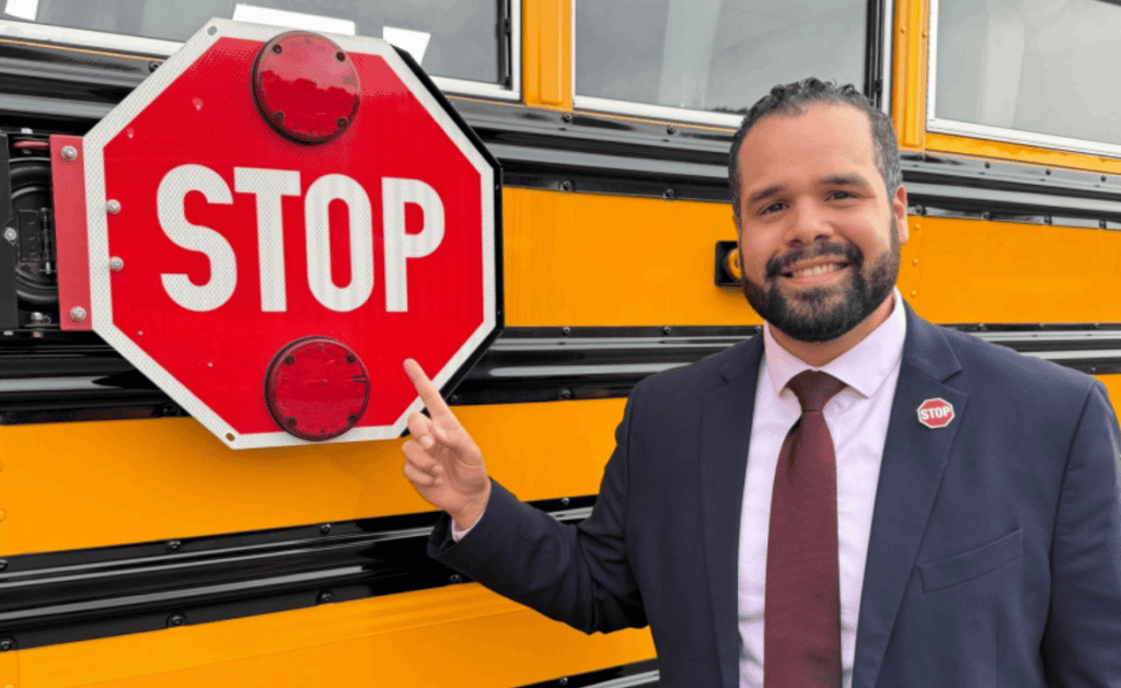 Man in suit pointing at school bus stop sign for safety awareness.