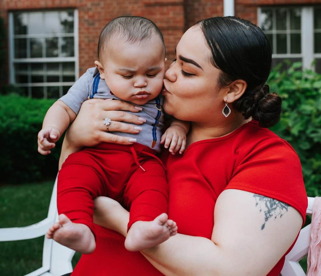 Mom holding and kissing her baby outdoors, promoting nutrition access for families.