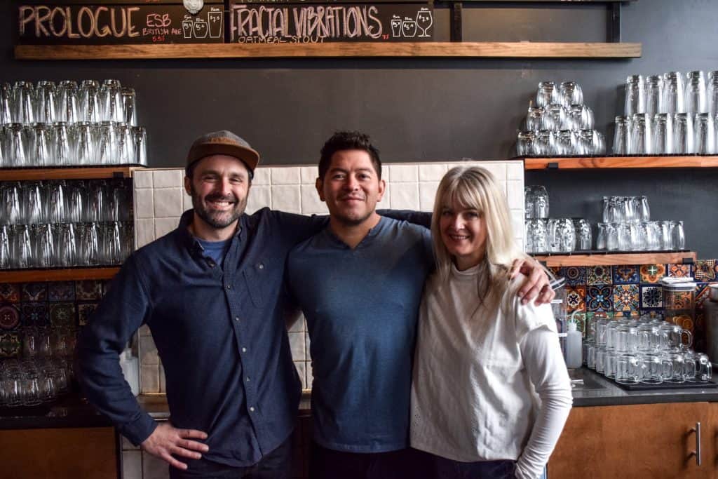 Ravenna Brewing, a Latino-owned brewery in Seattle, with three smiling staff members behind the bar.