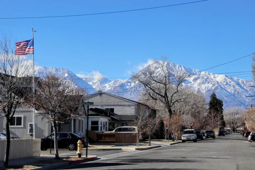 Snow-capped mountains behind a suburban neighborhood with trees and parked cars.