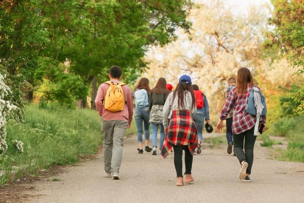 Latino immigrants walking outdoors in a park during daytime, carrying backpacks and wearing casual c.
