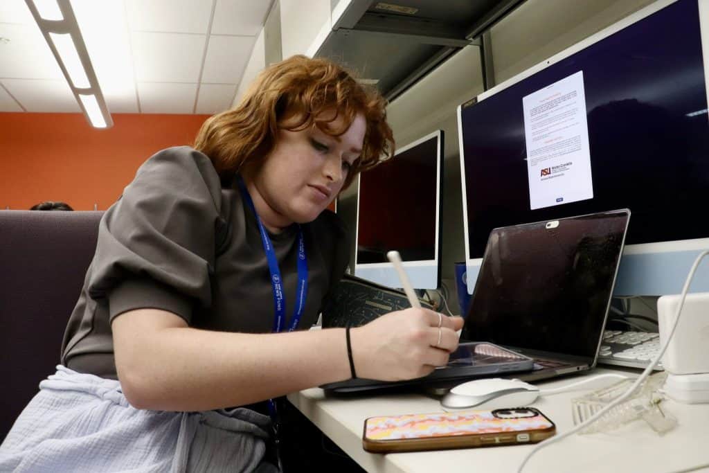 A woman working at a desk with multiple computer monitors, related to Latino News Network and NPR Mi.