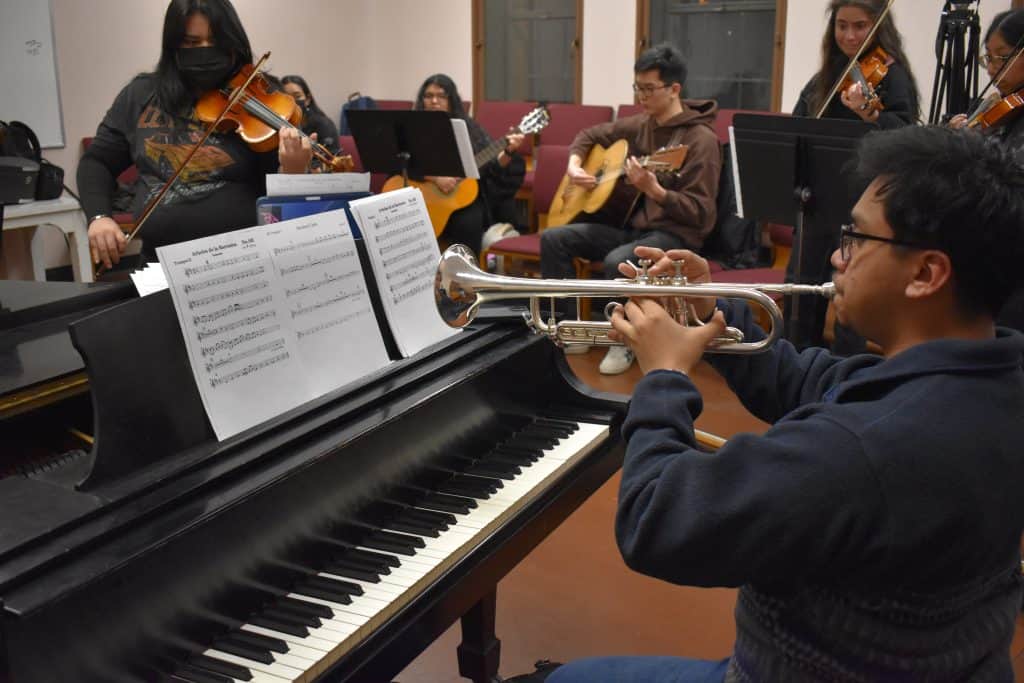 Young musicians playing trumpet, violin, and guitar during a rehearsal.