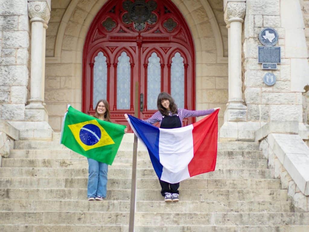 Brazilian and French students holding flags on university steps, promoting international student div.