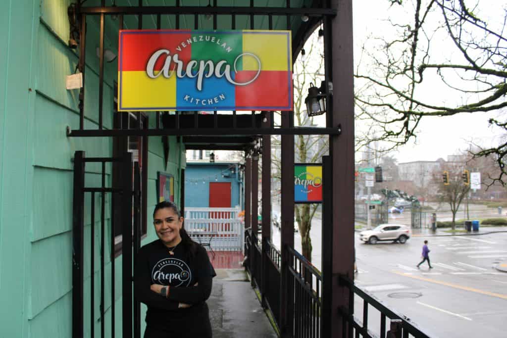 Venezuelan Arepa restaurant entrance with a smiling staff member outside.