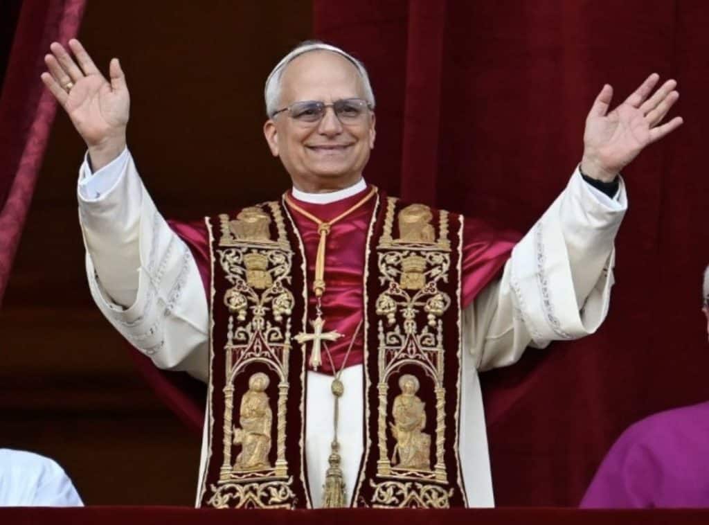 The American Pope in traditional papal vestments, smiling with arms raised during a religious ceremo.