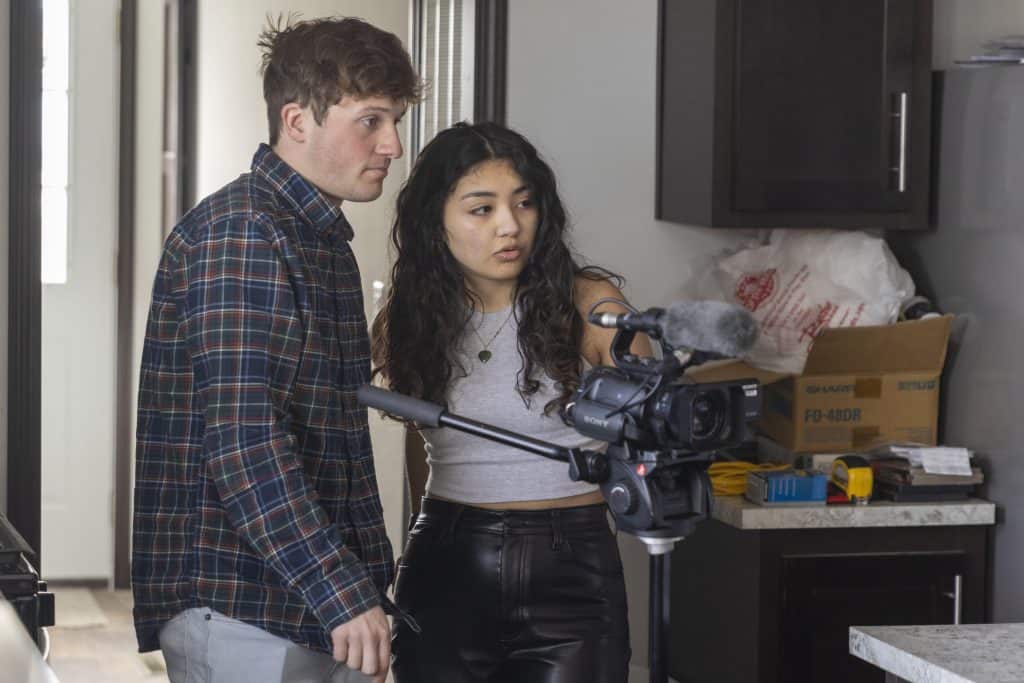 A woman and a man operating a professional video camera in a modern kitchen setting.