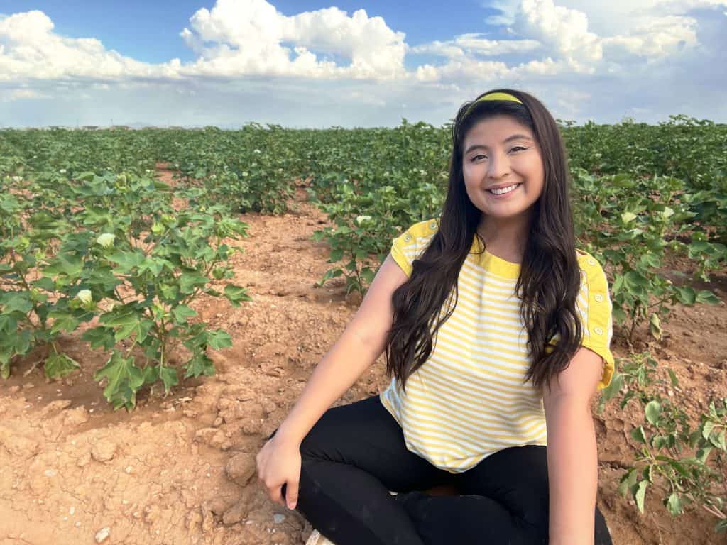 Young girl smiling in a cotton field, promoting bilingual education and cultural pride.