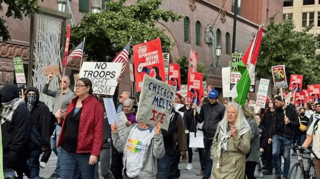 Protesters at a rally against immigration arrests and ICE policies in an urban setting.