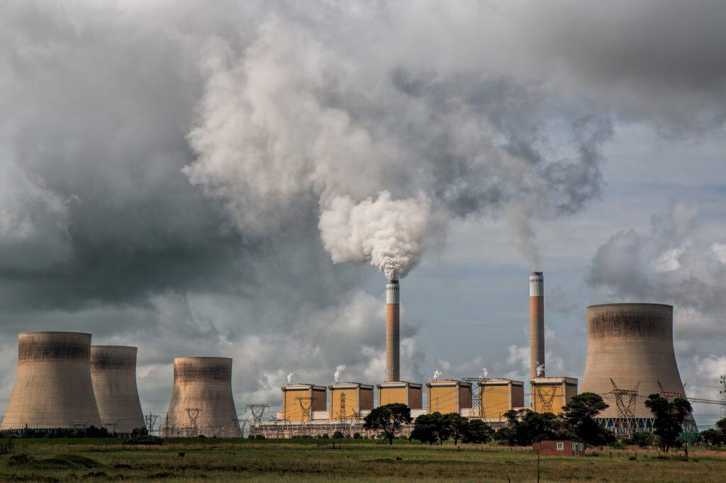 Power plant emitting smoke and steam in cloudy sky.