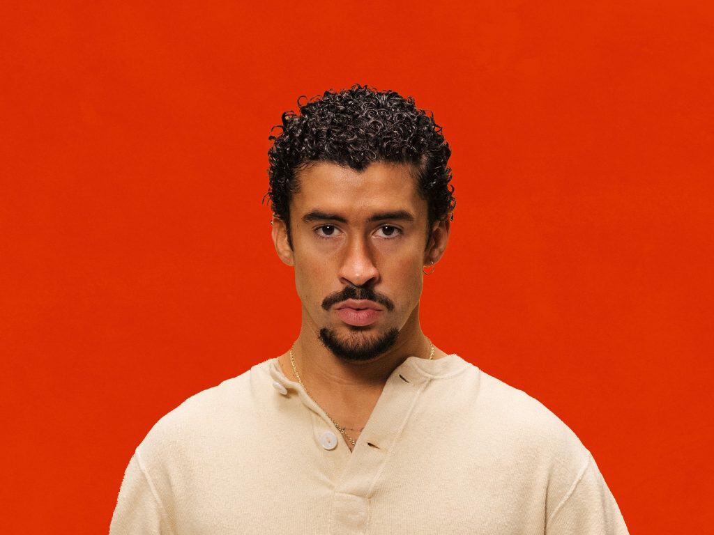 Empowered Latino man with curly hair against vibrant orange background, symbolizing leadership and c.