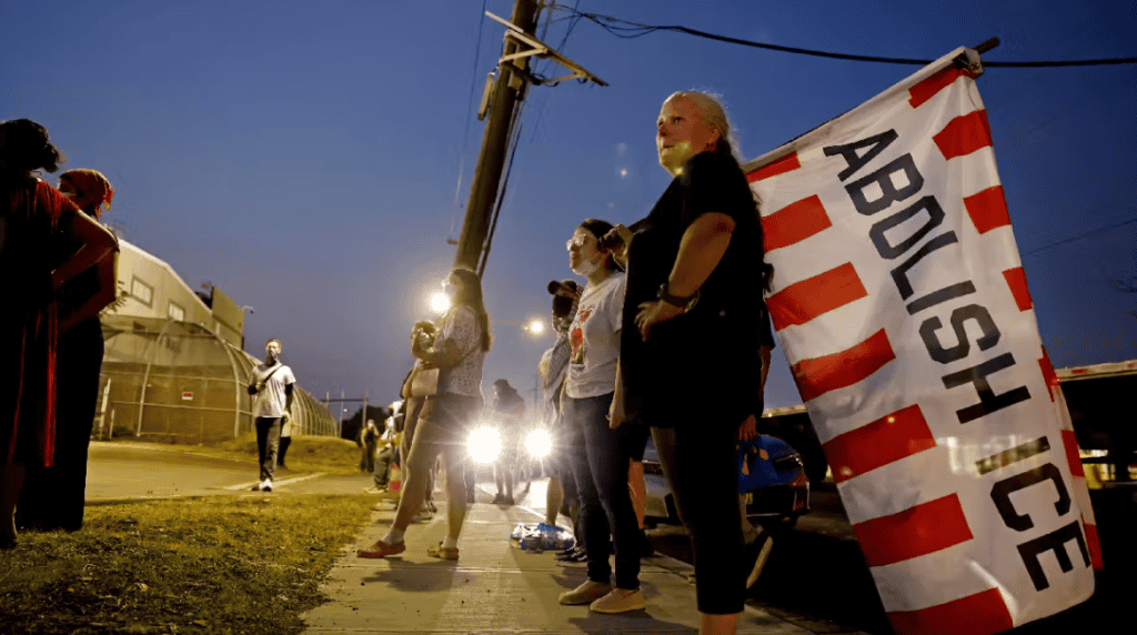 Protesters rally against immigration detention growth outside a courthouse at dusk.