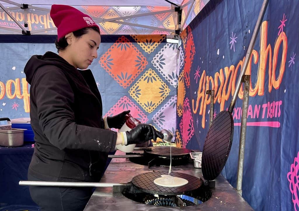 Latino woman cooking at a food stand with colorful decorations, promoting Latino culture and communi.