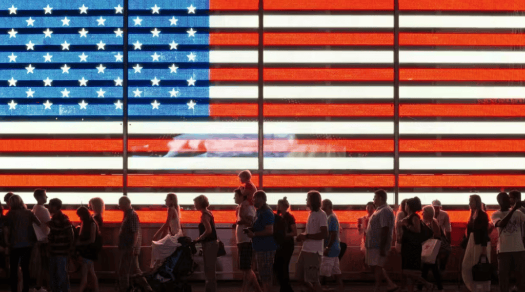 American flag display with diverse people walking in front, symbolizing immigration and unity.