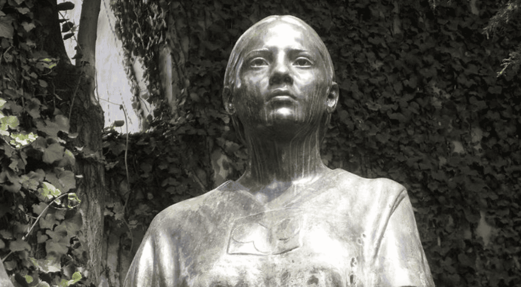 Bronze statue of a 16th-century Mexican woman with lush greenery background.