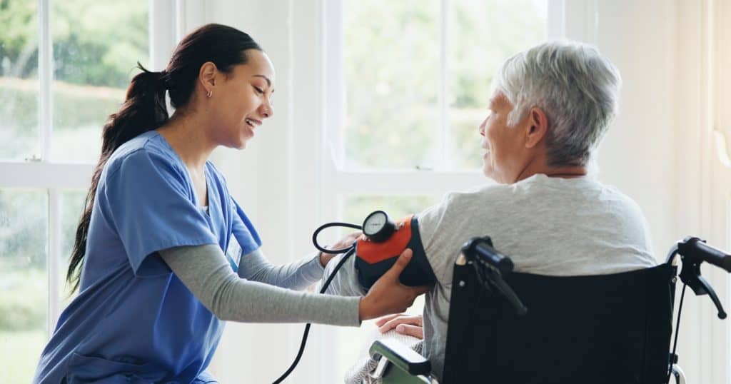 Hospice nurse checking blood pressure of elderly patient in wheelchair at home.