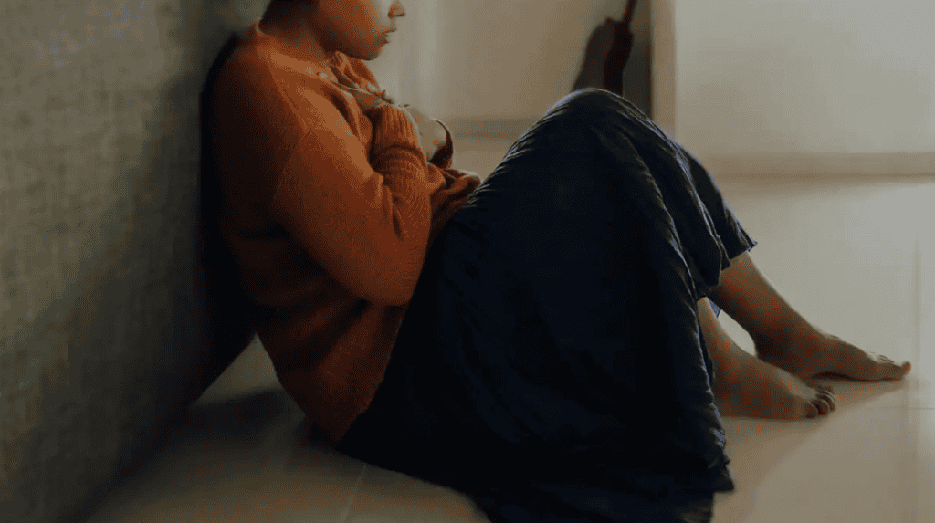 A young child sitting alone on the floor, looking contemplative and somber.