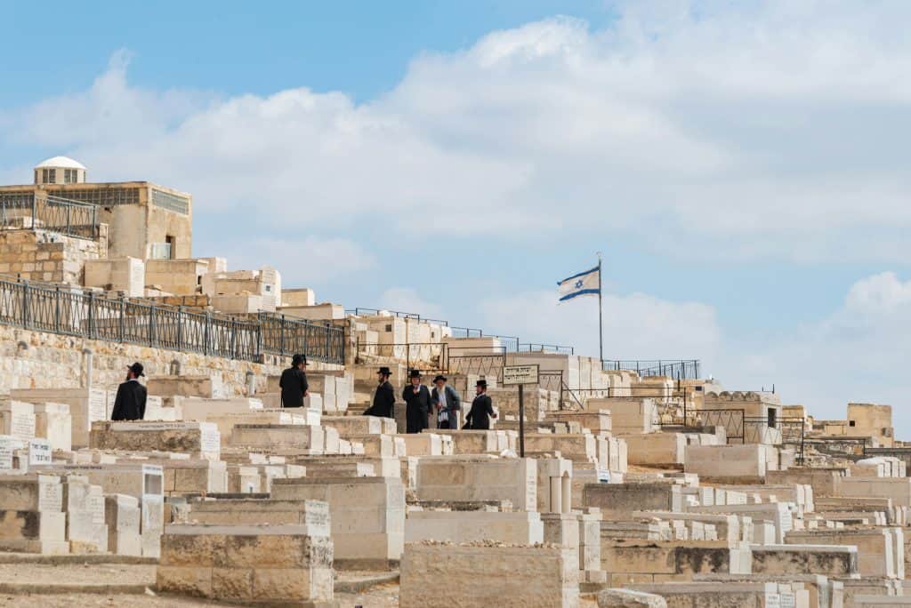 Orthodox Jewish men gather at Mount of Olives Cemetery in Jerusalem, Israel, under a clear sky.