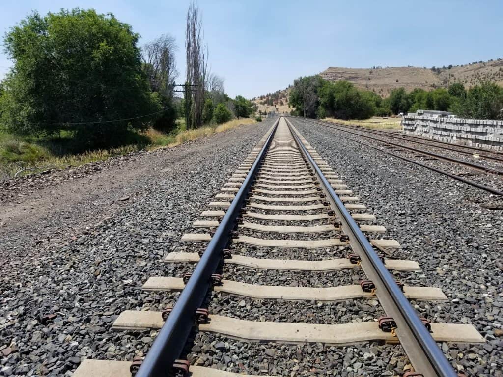 Railroad tracks stretching into the horizon surrounded by lush greenery in Oregon, USA.