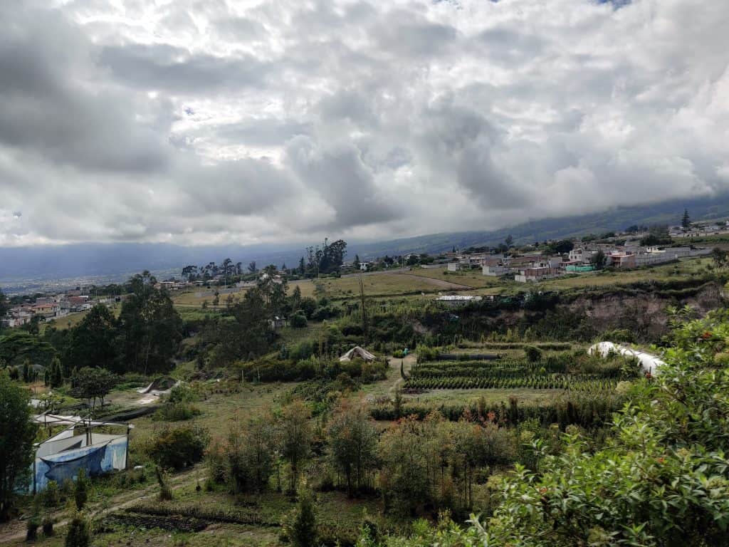 A lush rural landscape with cultivated fields and scattered houses under a cloudy sky.